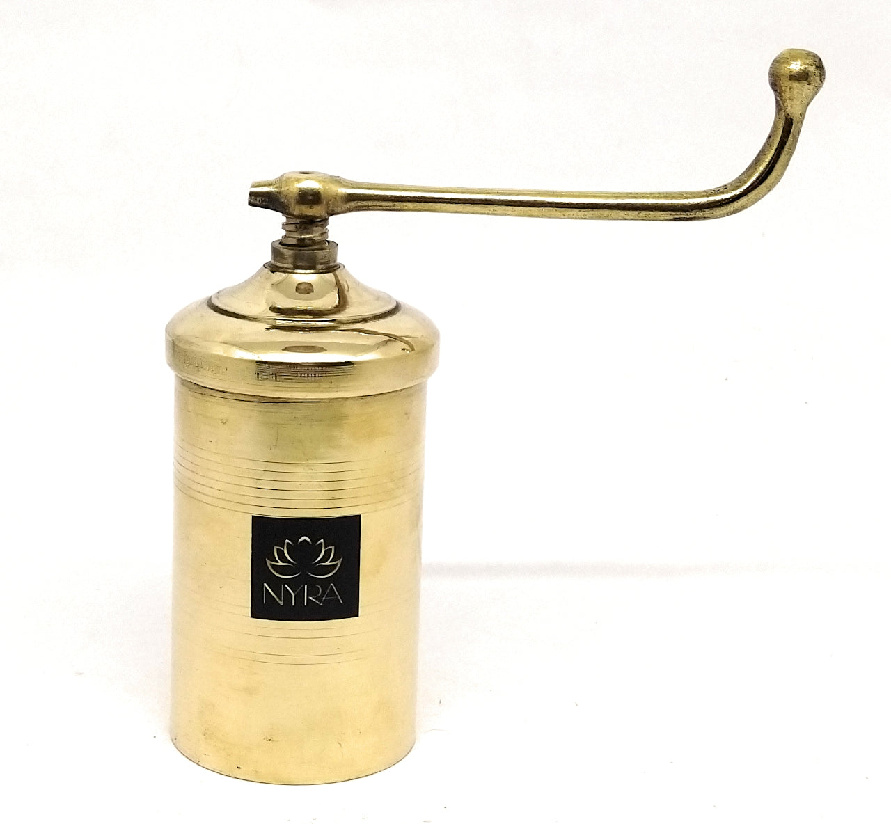 A brass manual coffee grinder with a curved handle, featuring a black square logo plate on the front that reads 'NYRA' with a lotus flower icon. The product is photographed on a clean white background.