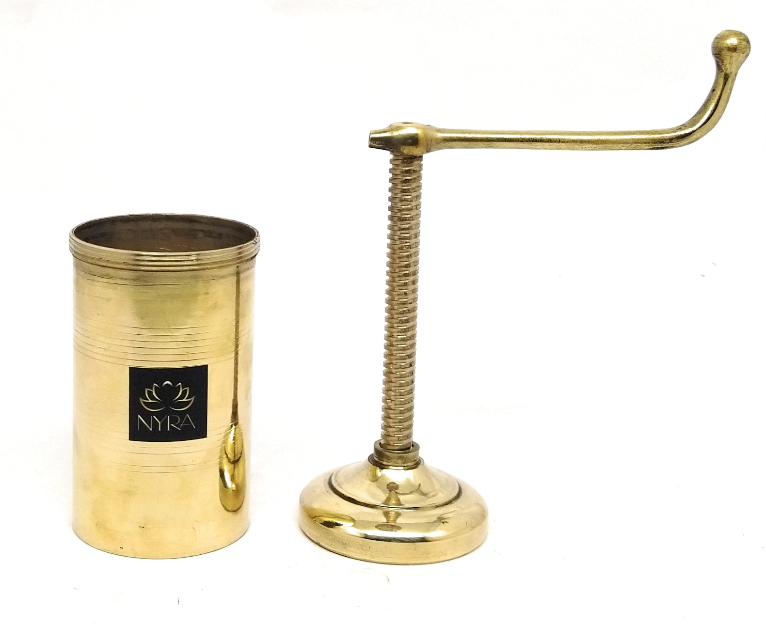 A brass manual coffee grinder shown next to its cylindrical storage container on a plain white background. The container features a black square label with the brand name 'NYRA' in white script.