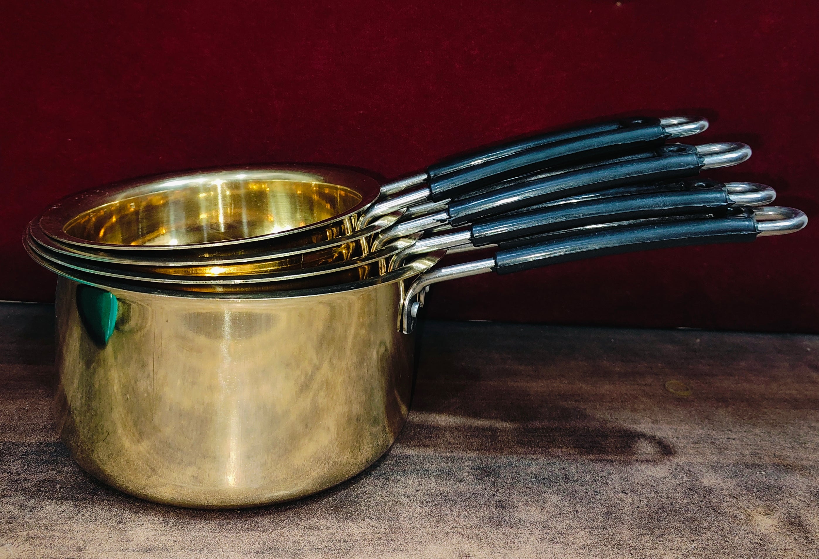 Set of brass measuring cups with blue handles on a dark surface