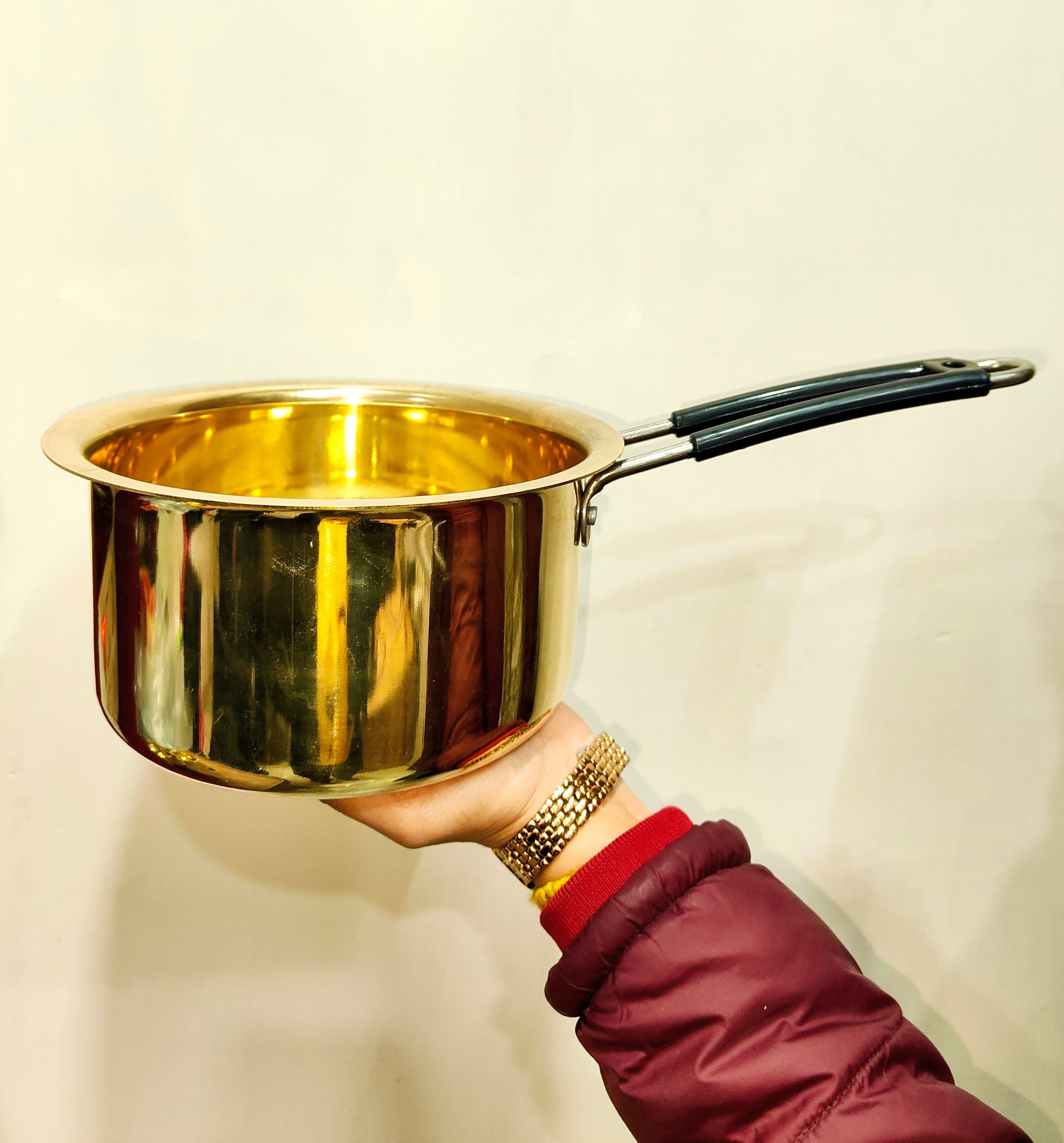 Gold-colored pot held by a person wearing a red sleeve against a beige background
