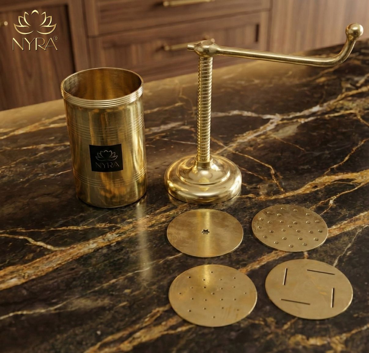 Gold kitchen utensils including a press and coasters on a marble surface with Nyra logo.