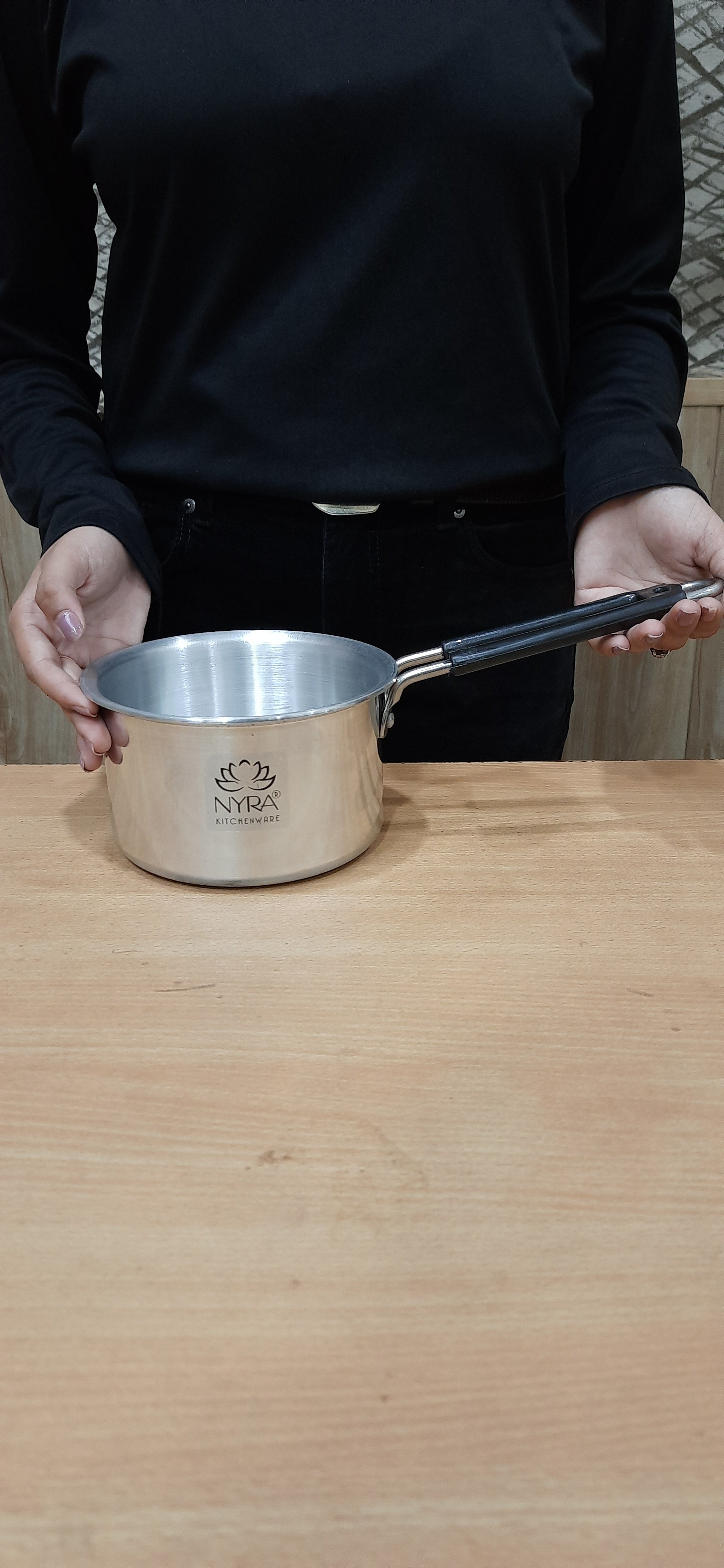 Person holding a metal spatula over a wooden surface with a visible brand logo.